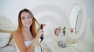 Graceful Young Woman Stacks Hair by Using Hair Styler Hair, Sitting on Chair