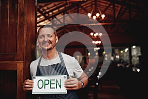 We gracefully invite you to join us. Portrait of a cheerful middle aged business owner holding up a sign saying open