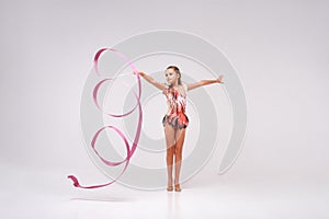 Gracefulness. Full-length shot of flexible cute girl child gymnast doing acrobatic exercise using ribbon isolated on a