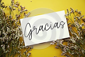 Gracias (Spanish language) text with flowers decoration on yellow background