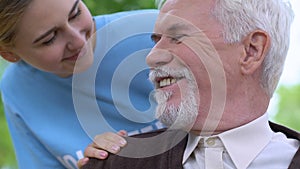 Gracious volunteer talking to disabled old man in wheelchair during park walk