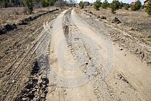 Grader rural road leading to the village. Dirt mud and dusty road through a field and trees against a clear blue sky, with tire