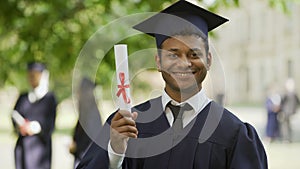 Graduate in academic dress and cap showing diploma and thumbs-up, education