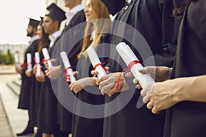 Graduate concept.Cropped image of row of students in black robes with diplomas in hands at graduation ceremony