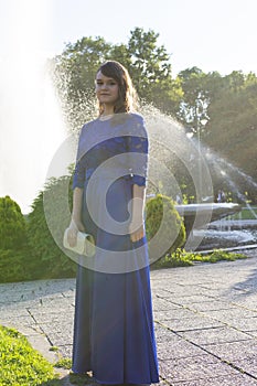 Graduate girl in blue fashionable dress at fountain background