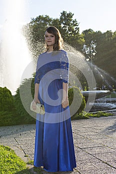 Graduate girl in blue fashionable dress at fountain background