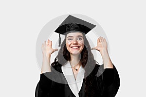 Graduate girl with master degree in black graduation robe and cap on white background. Happy young woman careerist have