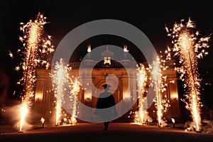 Graduate person in silhouette walking towards grand building with fireworks. Celebration, grandeur, majestic entrance