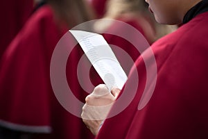 Graduate student nervously reading a piece of paper in hands or singing anthem