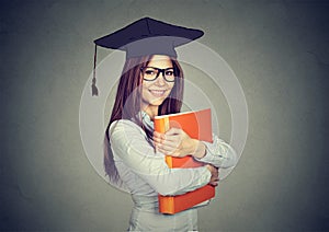 Graduate student woman in cap gown with folder looking at camera