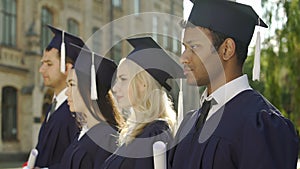 Graduate students in academic regalia standing in line and listening to speech