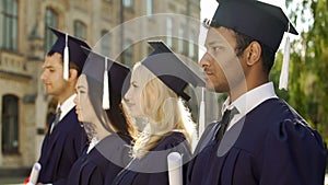 Graduate students in academic regalia standing in line and listening to speech