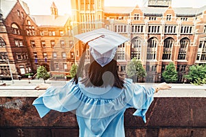 Graduated student girl in robe and hat looks into the future life after university standing on a rooftop at sunset time