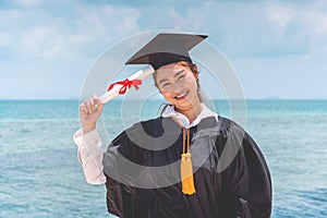 Graduated woman in cap and gown holding certificated celebrating in Commencement day with blue sky on the beach