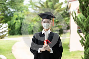 Graduated woman wear cap gown and  Medical mask for protection virus holding diploma or certificated due Virus outbrake
