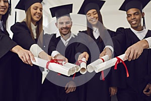 Graduates friends joining diplomas together as symbol of unity, common achievement, team, success