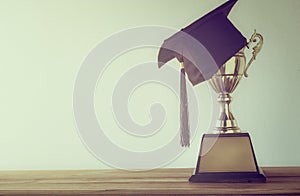 graduation cap with champion golden trophy on wood table with co