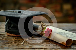 Graduation cap and diploma with red ribbon on wooden table with bokeh lights background