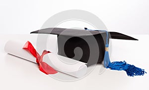 Graduation cap and diploma on white