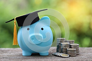 Graduation hat on blue piggy bank with stack of coins money on nature green background, Saving money for education concept