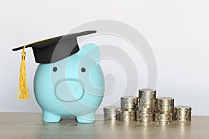 Graduation hat on blue piggy bank with stack of coins money on white background, Saving money for education concept