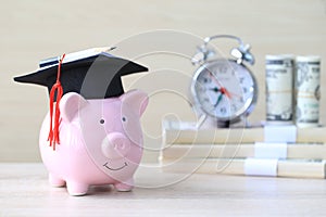 Graduation hat on blue piggy bank with stack of coins money on wooden background, Saving money for education concept