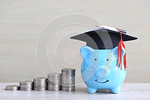 Graduation hat on blue piggy bank with stack of coins money on wooden background, Saving money for education concept