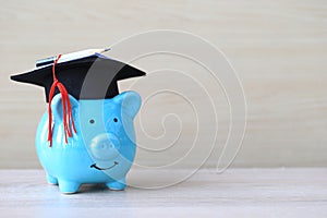 Graduation hat on blue piggy bank on wooden background, Saving money for education concept