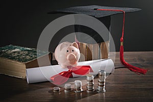 Graduation hat, book, diploma, coins and piggy bank on the wooden table