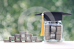 Graduation hat on coins money in the glass bottle on natural green background, Saving money for education concept