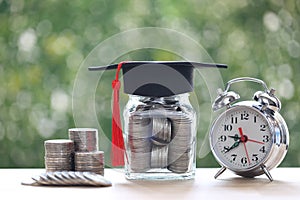 Graduation hat on the glass bottle and alarm clock on natural green background