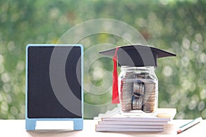 Graduation hat on the glass bottle and blackboard on natural green background, Saving money for education concept