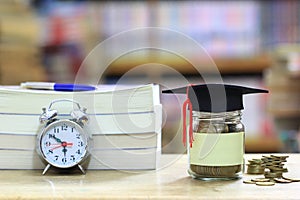 Graduation hat on the glass bottle on bookshelf in the library room background, Saving money for education concept