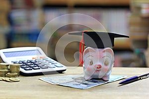Graduation hat on piggy bank on bookshelf in the library room background, Saving money for education concept