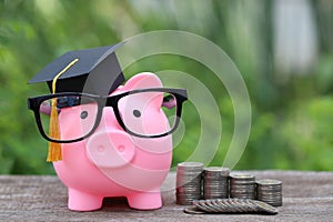 Graduation hat on pink piggy bank with stack of coins money on nature green background, Saving money for education concept