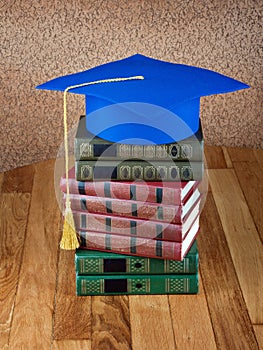 Graduation mortarboard on top of stack of books on wooden table