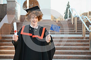 Graduation from university. Young smiling boy university graduate in traditional bonet and mantle standing and holding