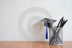 Graducate cap and black pencils on table with white wall background copy space - Back to school, education and scholarship