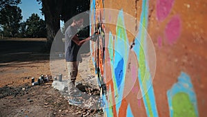 Graffiti artist painting on the street wall. Handsome Man with aerosol spray bottle spraying with colorful paint, Urban