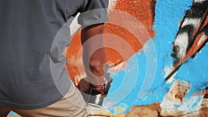 Graffiti artist painting on the street wall. Male hand with aerosol spray bottle spraying with colorful paint, Urban