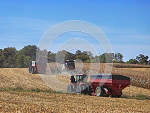 Grain cart being loaded from a combine harvester in  northern Illinois while a second tractor and grain cart wait