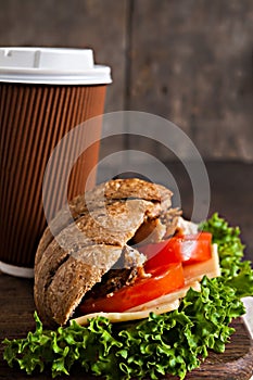 Grain croissant sandwich and a cardboard cup of coffee on a dark