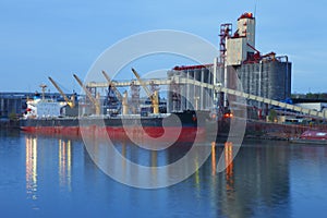 Grain elevators & cargo ship at dusk.