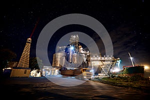 Grain terminal at seaport with starry sky on background. Cereals bulk transshipment from road transport to vessel at