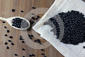 Grains black bean bag on side of wooden table, wooden spoon with black beans