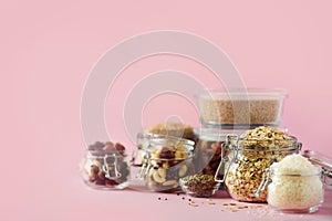 Grains, cereals, nut, dry fruits in glass jars over pink background with copy space. Clean eating, healthy, vegan diet concept