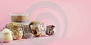 Grains, cereals, nut, dry fruits in glass jars over pink background with copy space. Clean eating, healthy, vegan diet concept