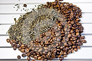 Grains of coffee and green tea leaves lie on a white table