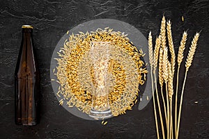 Grains and ears of malting barley near beer bottle on black background top view copyspace