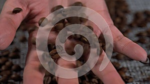 Grains fall into the woman's hand. Coffee beans on the table. Background consisting of roasted coffee beans.